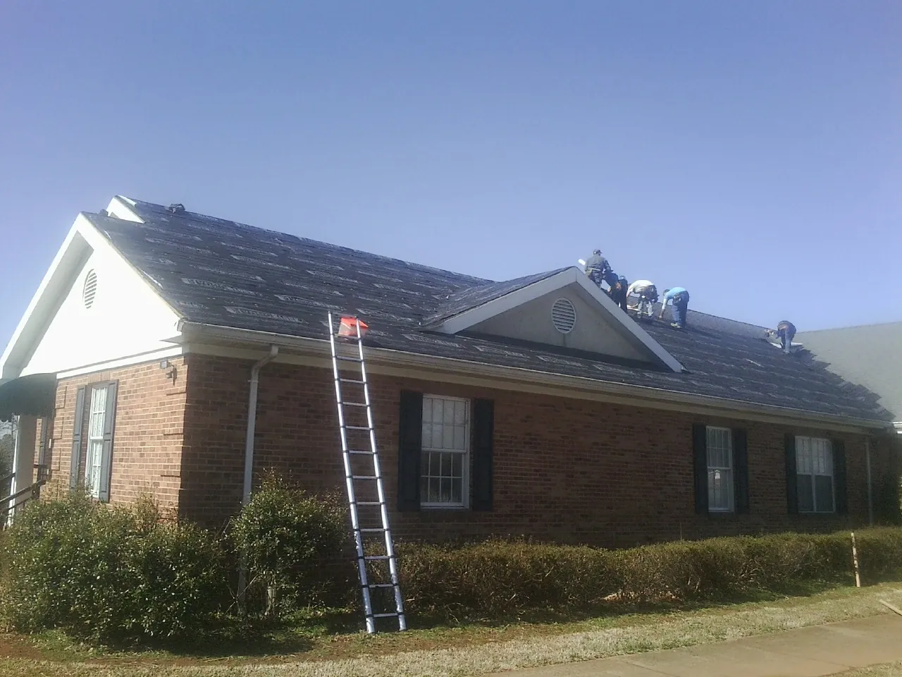 Crew tearing shingles off a brick ranch roof with a ladder set — Metal Roof Repair work by our crew in Sun Valley