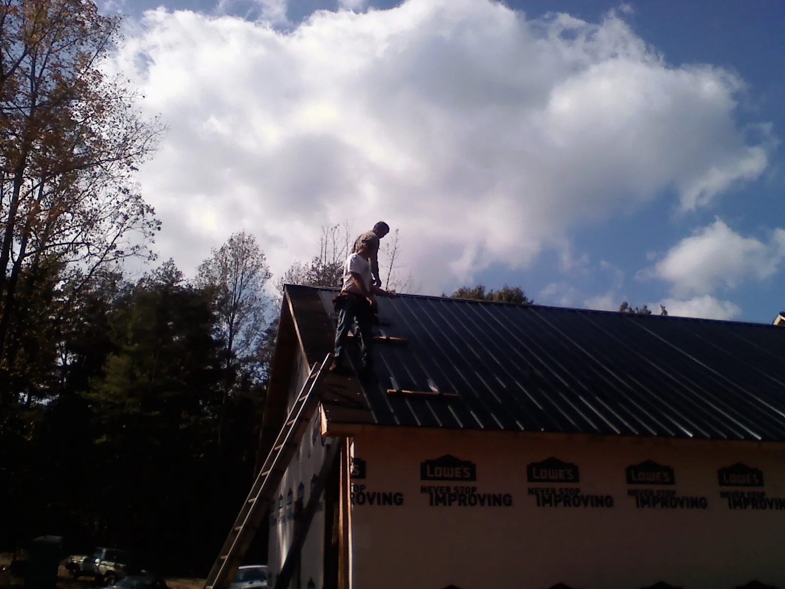 Roofer fastening dark metal panels high against a cloudy sky, from a Roof Inspection job in Sun Valley